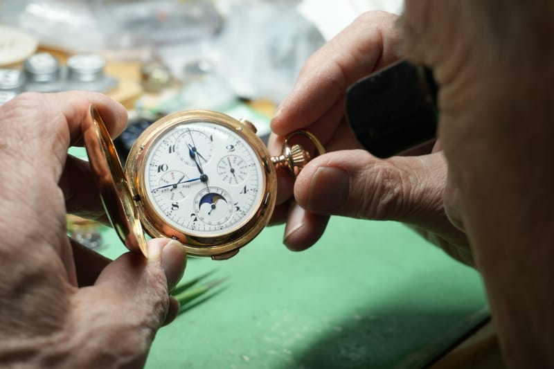 Hände des Uhrmachermeisters mit einer goldenen Taschenuhr mit Mondphase in der Werkstatt