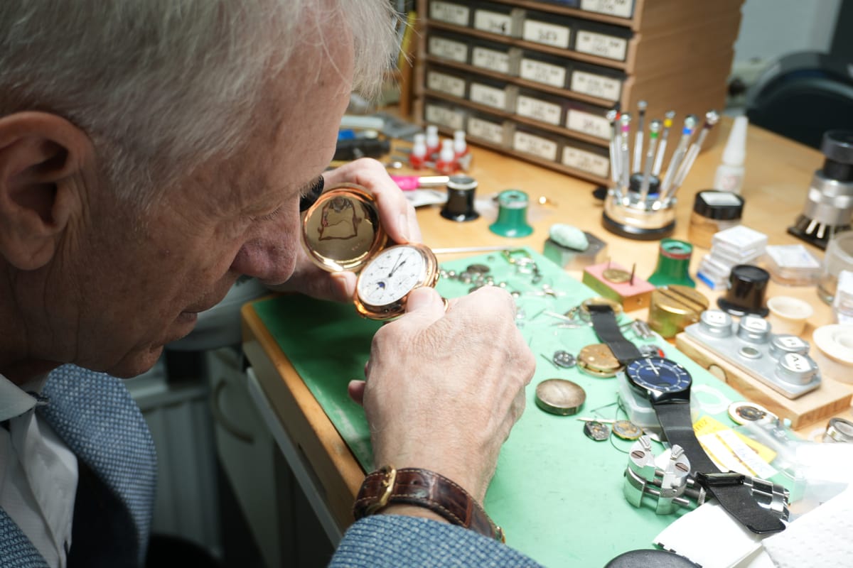 Der Uhrmachermeister prüft eine Taschenuhr mit der Lupe an seiner Werkbank